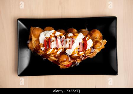 A black plate with wafer cookies, ice cream, and fresh strawberries on a wooden background Stock Photo