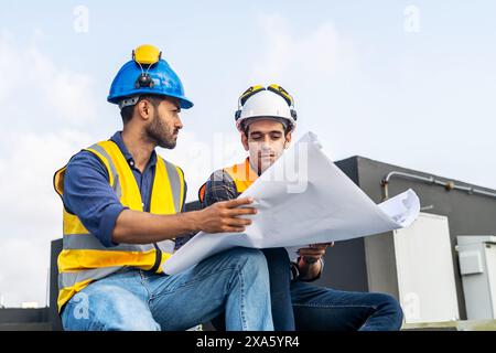 The two workers in hard hats examining architectural plans on a rooftop in Thailand, Bangkok Stock Photo