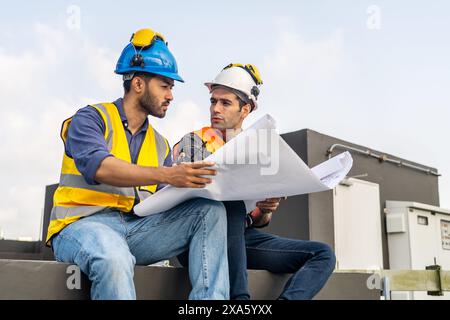The two workers in hard hats examining architectural plans on a rooftop in Thailand, Bangkok Stock Photo