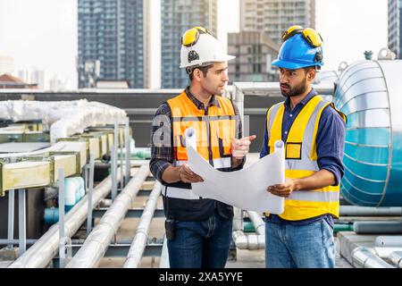 The two workers in hard hats examining architectural plans on a rooftop in Thailand, Bangkok Stock Photo