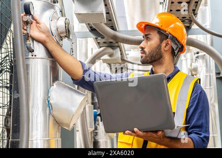 A man using a laptop in a manufacturing plant to work on a project in Thailand, Bangkok Stock Photo