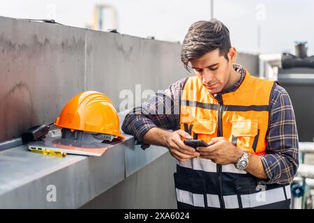 A man in work attire checks his phone in a factory setting in Thailand, Bangkok Stock Photo