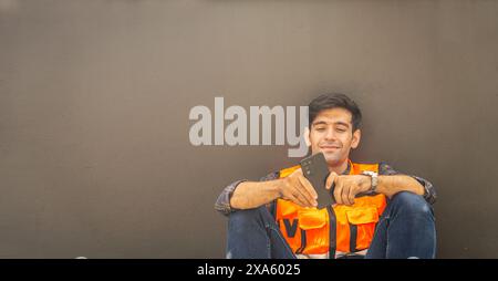 A smiling man in an orange vest using his phone Stock Photo