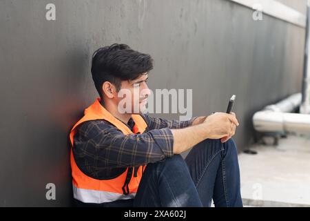 A smiling man in an orange vest using his phone Stock Photo