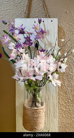 The wall hanging pink and purple artificial flowers in a vase on a wooden board for a country vibe decoration Stock Photo