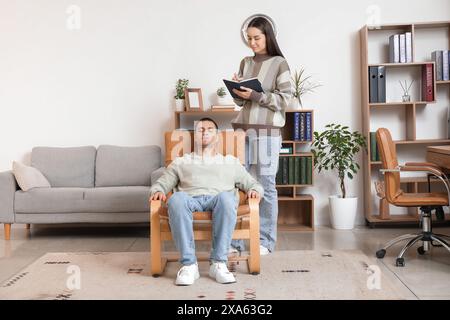 Female psychologist with notebook and hypnotized man in office Stock Photo