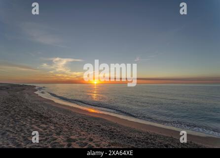 The sunrise on the beach of Mojacar is presented with a golden sky and the sun's rays shining on the sea. The beach, of fine sand and brown color. Stock Photo