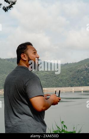 Bearded man looking up to the sky when flying drone near the lake. Viewed from behind. Stock Photo
