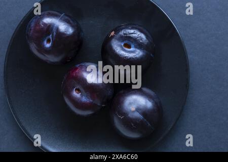 close-up tabletop photo of dark blue plum fruits in a black ceramic plate on a dark background, low key food still life photography Stock Photo