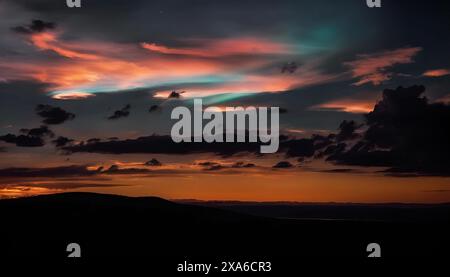 Vibrant nighttime sky with clouds in orange, blue, and green hues over mountain Stock Photo