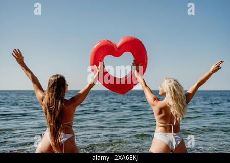 Two women are holding a red heart shaped inflatable raft in the ocean Stock Photo