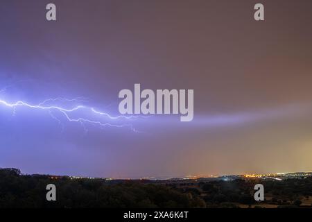 A spectacular night storm dominates the sky, marked by significant lightning, while on the horizon the lights of the big cities illuminate. Stock Photo