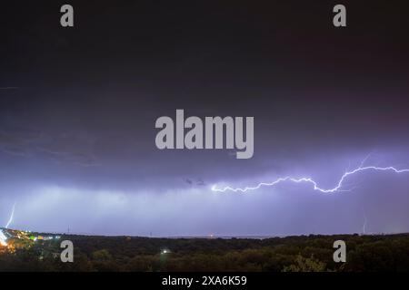 A spectacular night storm dominates the sky, marked by significant lightning, while on the horizon the lights of the big cities illuminate. Stock Photo