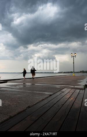 A Father and son fishing off a pier during stormy weather with dramatic clouds over the lake Stock Photo