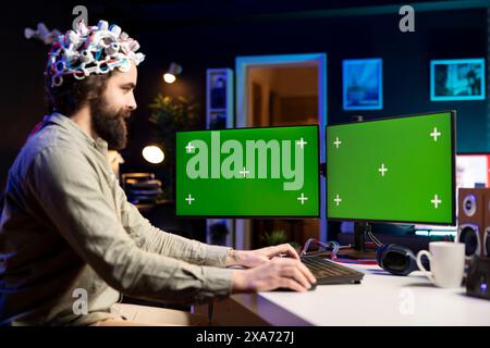 Neuroscientist using EEG headset and isolated screen multi monitor setup to upload mind into computer. Engineer using chroma key PC, experimenting with transferring consciousness into cyberspace Stock Photo