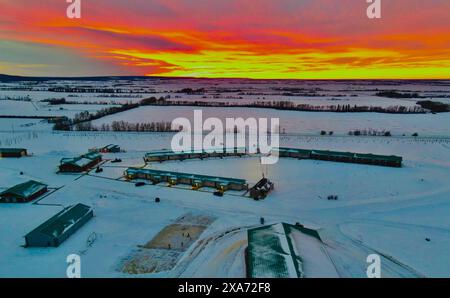A sunset setting over a snowy farm field Stock Photo