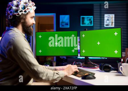 Happy developer using EEG headset device translating thoughts into isolated screen desktop PC commands. Smiling IT specialist controlling mockup multi monitor computer functions using mind Stock Photo