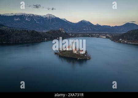 Bird&#39;s eye view of St. Mary&#39;s Church in Lake Bled and snowy mountains just after sunset in Bled, Slovenia, Europe. Stock Photo