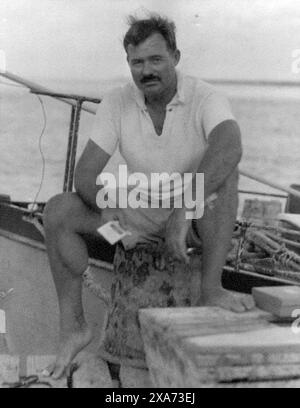 1930s Ernest Hemingway sitting on a dock next to the Pilar, 1930s.  Kennedy Library Stock Photo