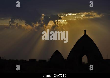 Sun rays shining through clouds in a silhouette image during sunset Stock Photo