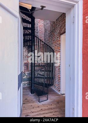 Looking through the doorway of Fisgard Lighthouse to the black wrought iron staircase leading up, surrounded by red brick walls. Stock Photo