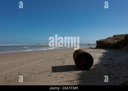 An abandoned barrel rests on a sandy beach by the sea Stock Photo