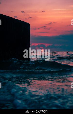 Sunset reflecting on ocean waves crashing with a sea wall in the foreground Stock Photo