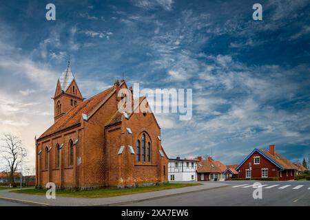 A large terracotta building of a church under blue cloudy sky next to red and white houses Stock Photo