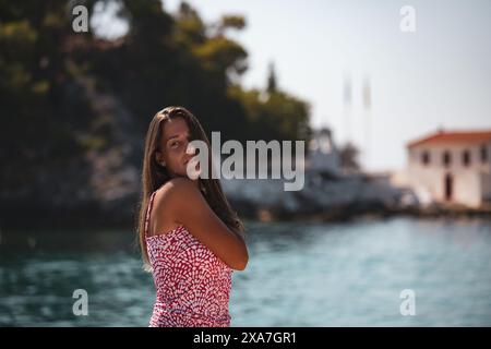 A woman in a pink dress standing by water, making eye contact with the camera Stock Photo