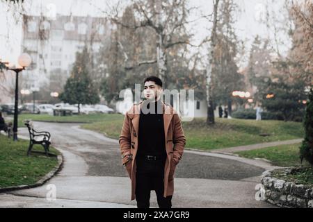 A man in stylish black turtleneck and brown coat standing on sidewalk Stock Photo