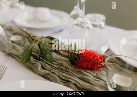 An elegantly set wedding table with glasses and a vibrant red flower centerpiece Stock Photo