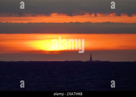 Sun setting behind lighthouse over water and clouds Stock Photo