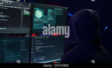 Dangerous man hacking, stealing credit card numbers and infiltrating banking systems, handheld camera shot. Close up of hacker running code in apartment on PC monitors, camera B Stock Photo