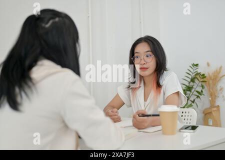 A young, friendly Asian female college student is helping her friend with math homework at a cafe. people and education concept Stock Photo