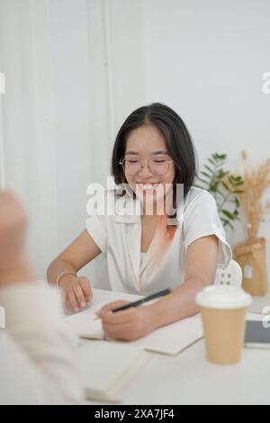 A young, friendly Asian female college student is helping her friend with math homework at a cafe. people and education concept Stock Photo