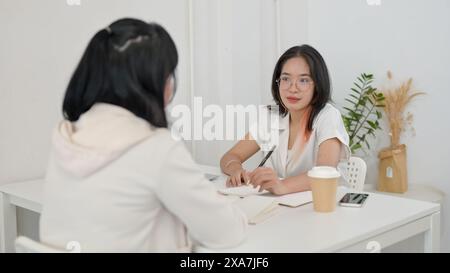 A young, friendly Asian female college student is helping her friend with math homework at a cafe. people and education concept Stock Photo