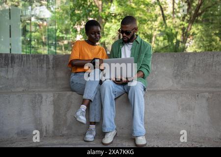 Thoughtful boyfriend, girlfriend classmates using computer to study sitting on campus stairs outside Stock Photo