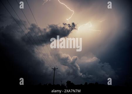 Dark stormy sky with lightning passing through clouds, silhouette of wires in background Stock Photo