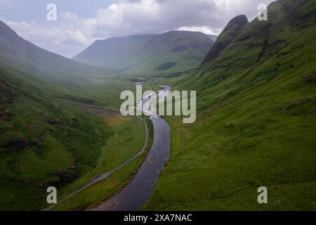 A winding road meandering through lush green mountains and rivers Stock Photo