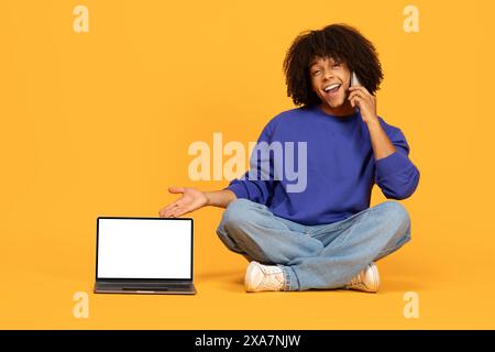 Young Guy Talking on Phone and Gesturing to Laptop Stock Photo