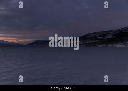 The Sun setting over snow-covered field with mountains in the background Stock Photo