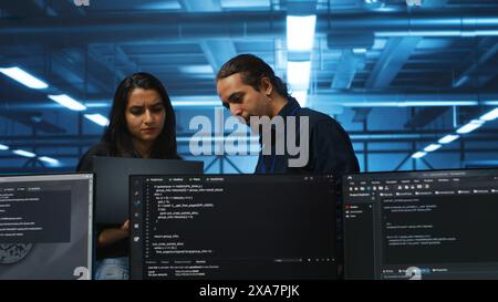 Developer in server hub using laptop to present manager plan of repairing equipment storing datasets. Specialist uses notebook to explain team leader ways of fixing rigs doing computational operations Stock Photo