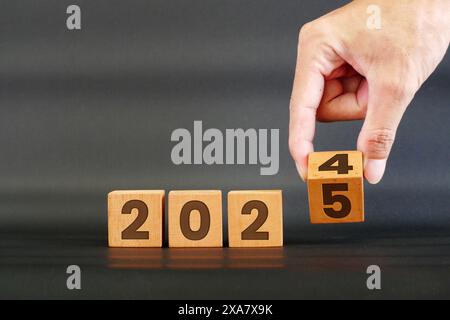 Hand flipping the years 2024 to 2025 on wooden cubes. Merry Christmas and New Year 2025 concept. Stock Photo