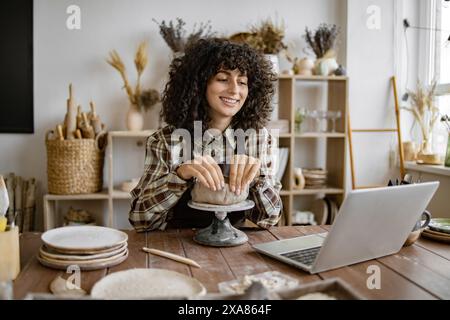 Woman shaping pottery while using laptop in studio Stock Photo