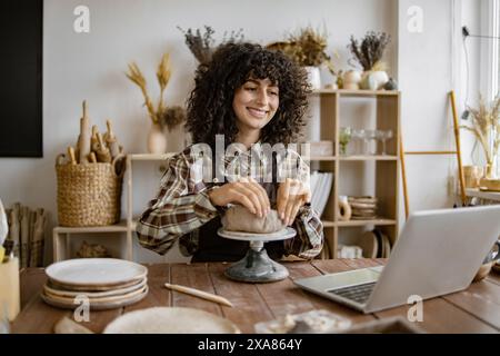Woman working on pottery using laptop in ceramic studio Stock Photo