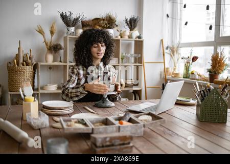 Young woman making pottery while using laptop in studio Stock Photo