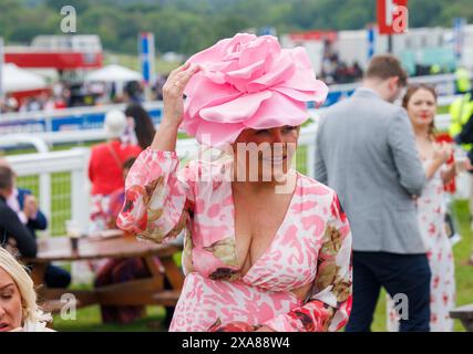 A woman holds on to her hat ins blustery conditions at the Epsom Derby festival. Derby Day at Epsom, one of the great races in the world. Stock Photo