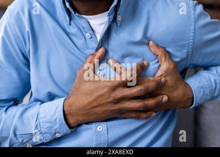 Man suffering from chest pain holding his chest with both hands, wearing a blue shirt. Close-up on the hands and chest. Stock Photo