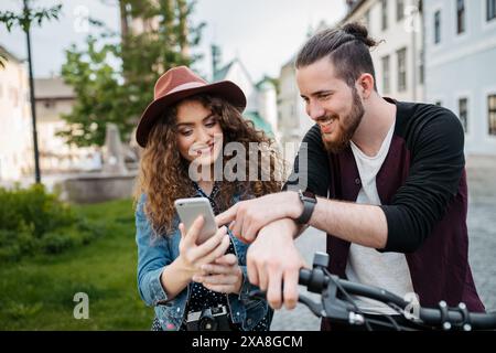 Travellers couple checking route in map app, standing by electric scooters in small city, sightseeing. Young tourist using bikes during their summer Stock Photo