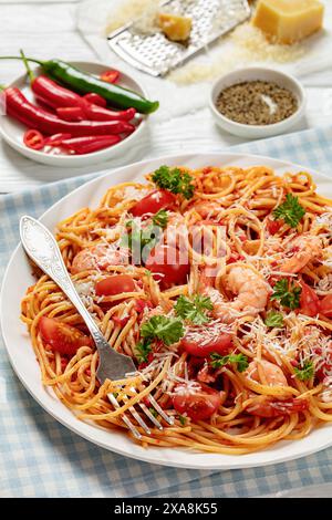 shrimp fra diavolo with spaghetti, tomato based hot sauce sprinkled with grated parmesan cheese on white plate on white wooden table with fork, vertic Stock Photo